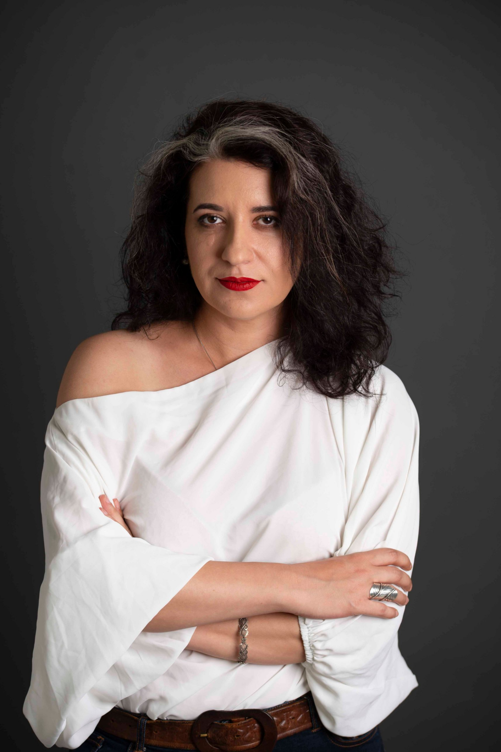 Adriana Tica, arms crossed, in a white top against a dark grey backdrop
